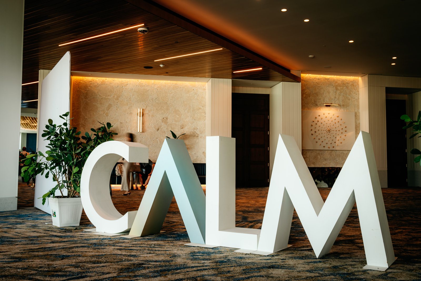Giant freestanding white CALM letters in the prefunction foyer, with plants and a wood ceiling