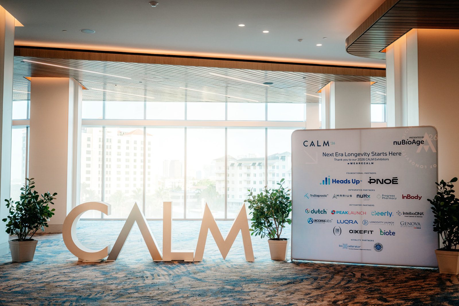 The CALM letters with potted plants beside the printed sponsor board, in front of floor-to-ceiling windows