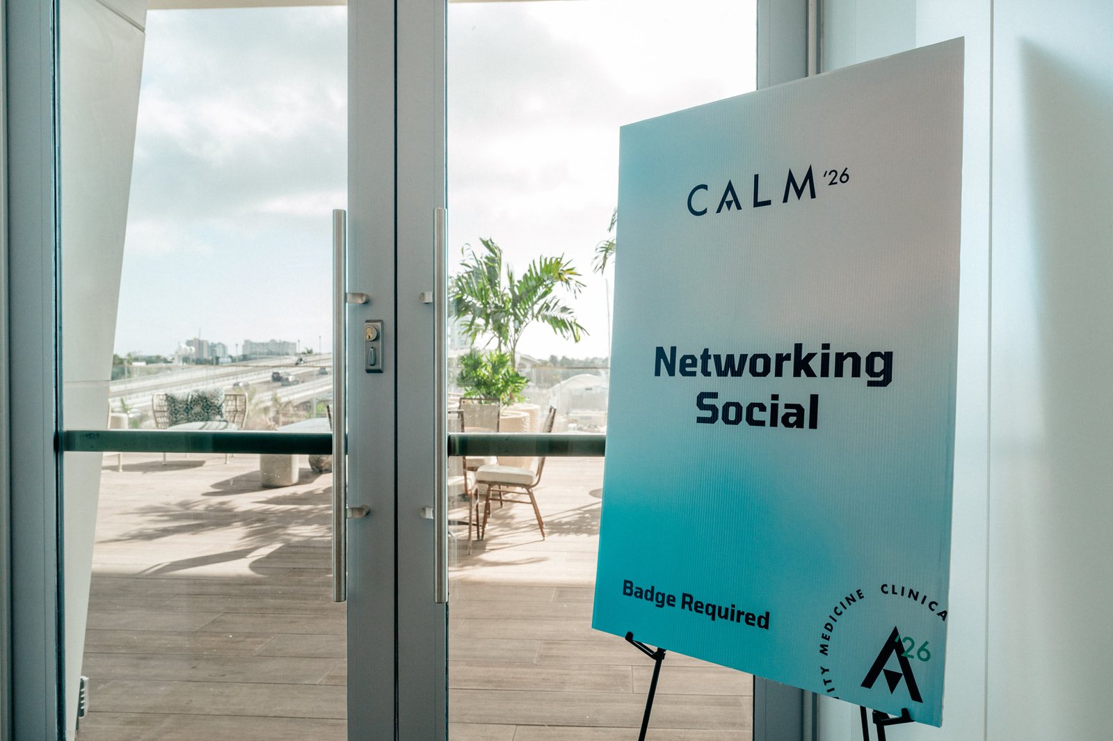 A printed CALM '26 Networking Social sign on an easel by glass doors that open onto a terrace