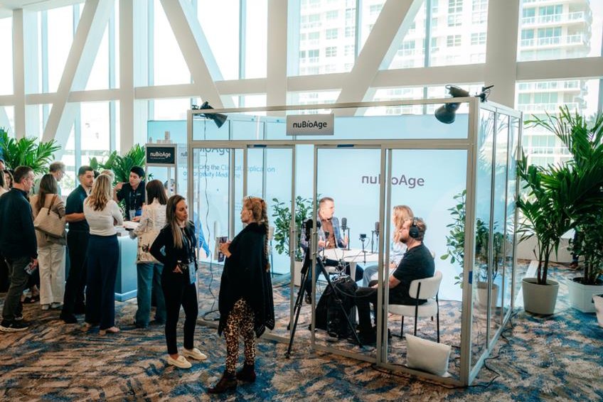The nuBioAge activation: glass-walled pods with interviews being filmed, in a bright prefunction space with palms
