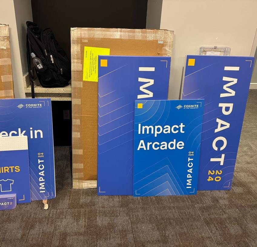 Printed boards for a tech conference stacked against a wall before install: check-in, arcade and tall feature signs
