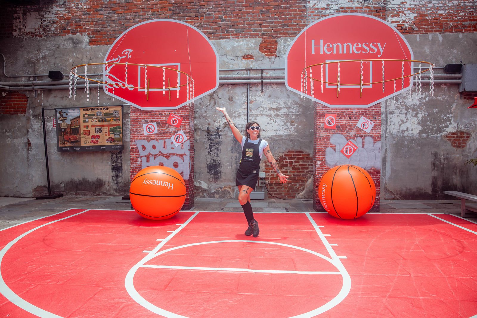 The double-hoop wall square-on, giant balls resting on the printed red half-court, one guest for scale