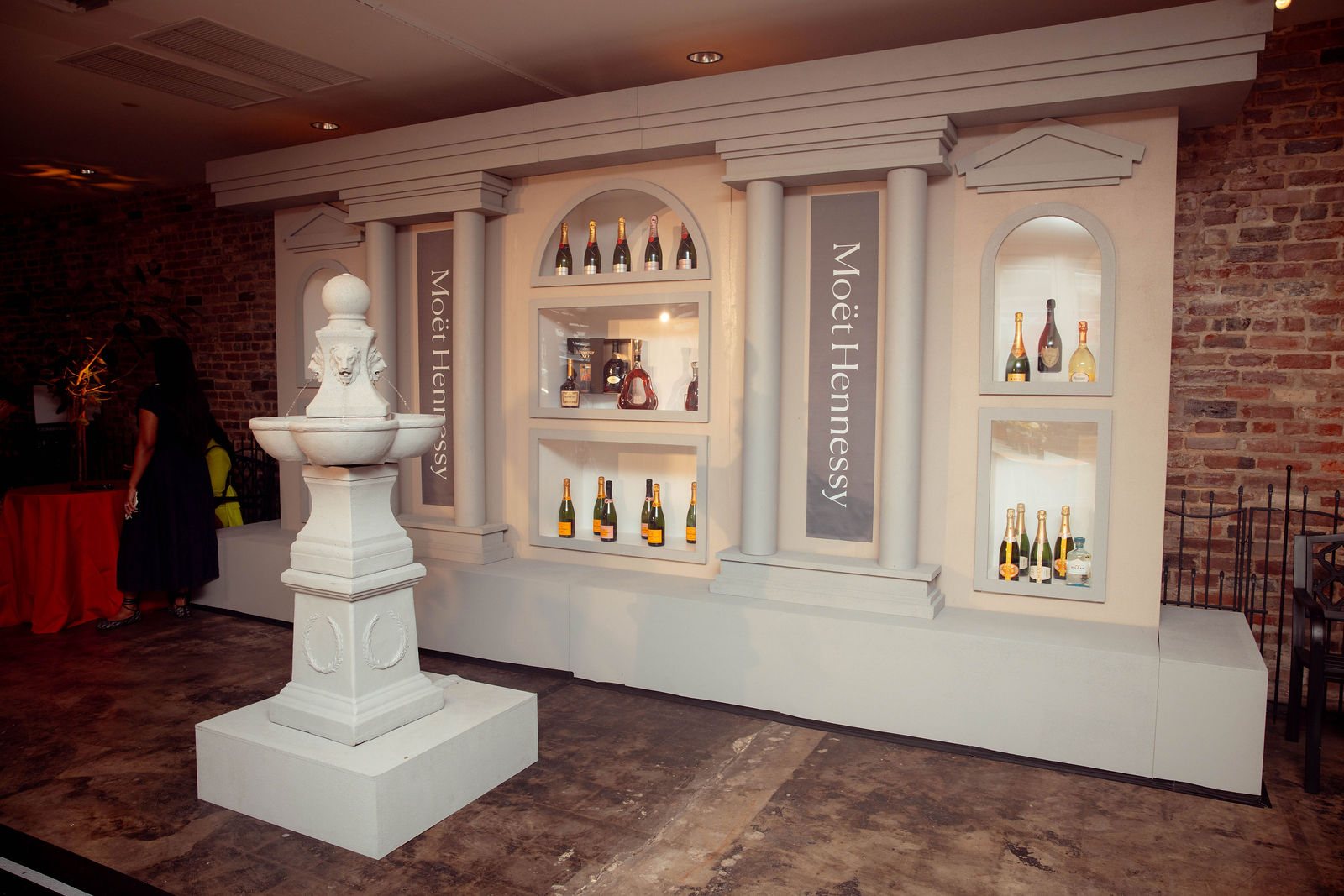 The stone-look facade in full: columns, lit niches holding bottles, the Moët Hennessy banners, and the scenic fountain in front