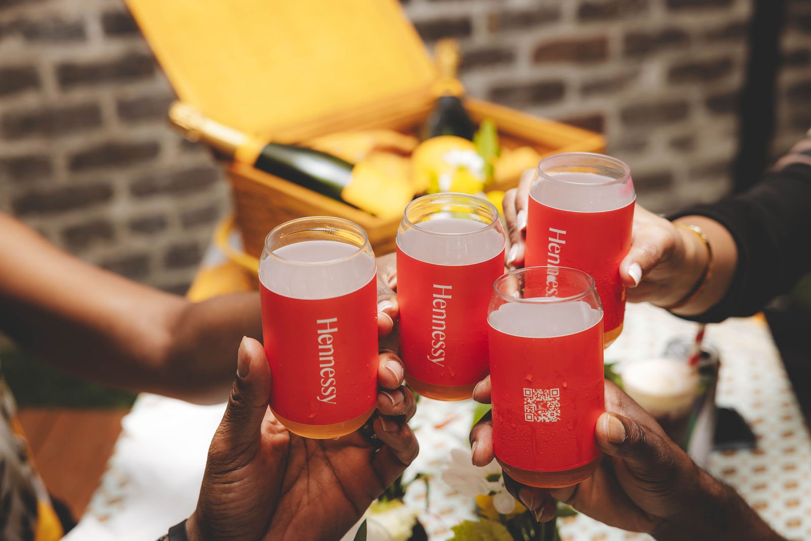 Four printed red Hennessy cups raised in a toast over a picnic basket