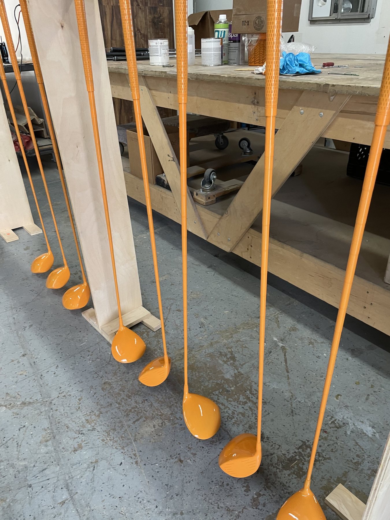 Oversized golf drivers painted glossy orange, standing beside a workbench in the Kenner shop