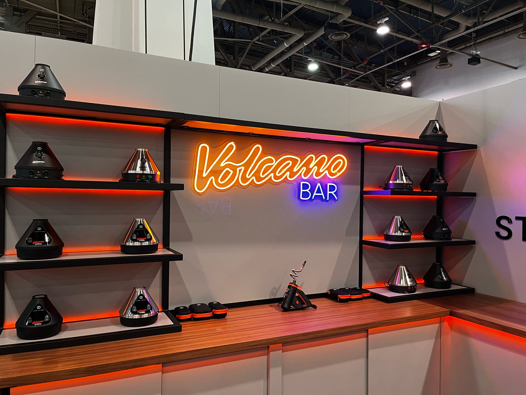 The Volcano Bar neon over lit black shelving holding the Volcano and Crafty product line, above a wood counter