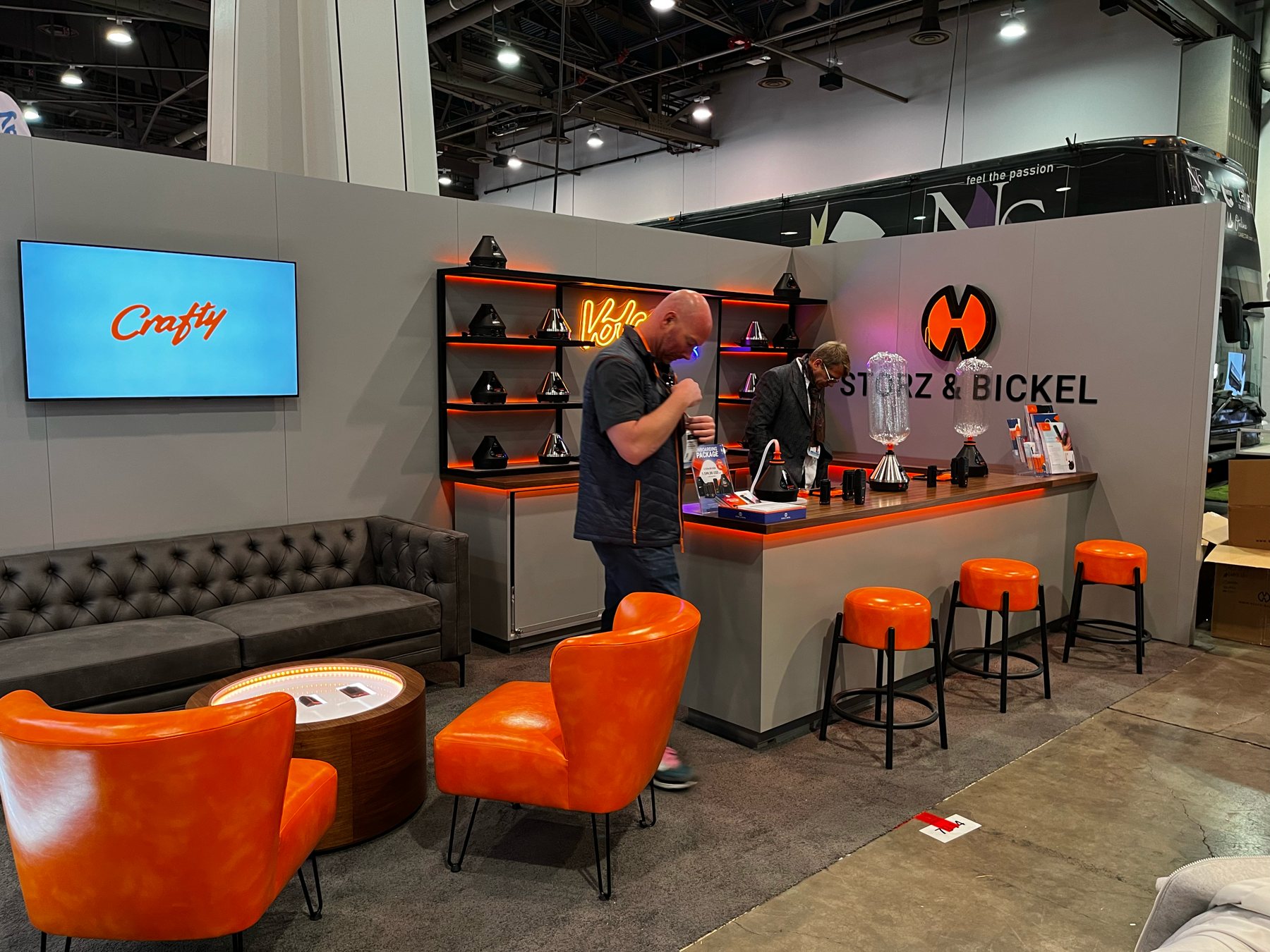 Setup finished on the Storz & Bickel booth: the counter with staff at work, the Crafty screen, orange stools and the lounge