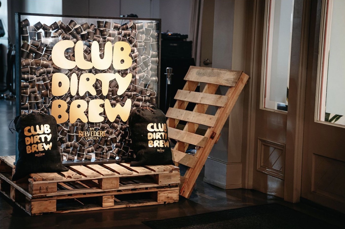 A framed glass case full of branded cups, standing on pallets with two burlap bags in front