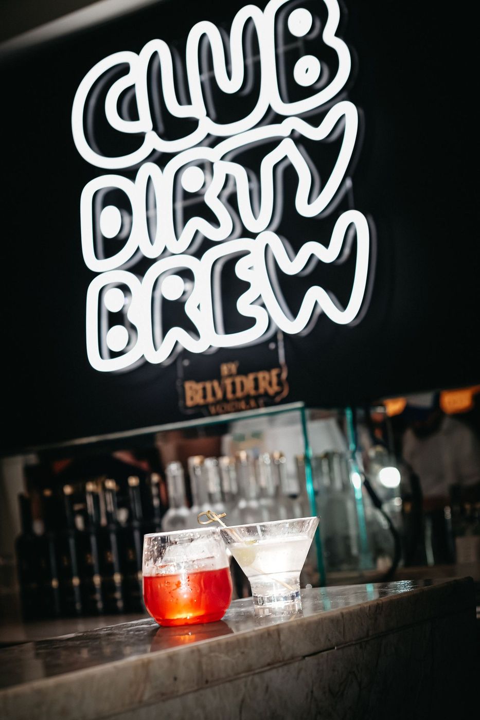 The CLUB DIRTY BREW custom neon sign lit white over a drinks station
